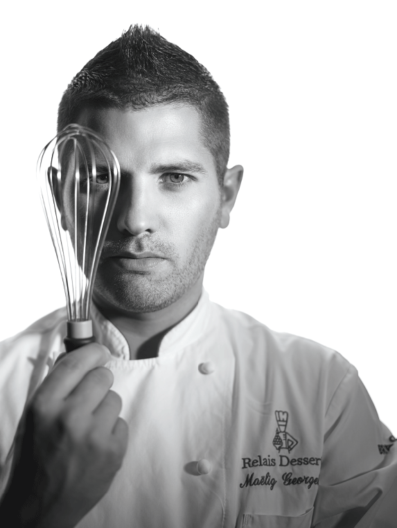 Chef Maëlig Georgelin poses with a pastry whisk. He is wearing a Relais Desserts International apron.